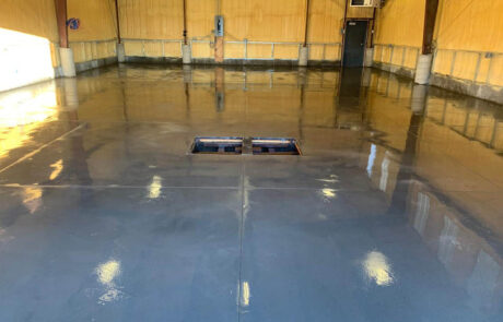 A large, empty warehouse with shiny, newly finished concrete floors. There is an open rectangular pit in the center of the floor, and the walls are lined with light wood paneling and structural beams. A large, empty warehouse with shiny, newly finished concrete floors. There is an open rectangular pit in the center of the floor, and the walls are lined with light wood paneling and structural beams.